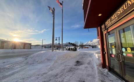 Flags unfurled in the wind outside Valdez Museum in February 2025 under a blue sky.
